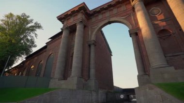 Güzel dizayn edilmiş tarihi bir bina, açık günbatımı gökyüzünün altında büyük sütunlar ve zarif kemerler sergiliyor.