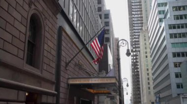 NEW YORK, ABD - 4 Nisan 2024: Bir Amerikan bayrağının gökdelenlerin arasında gururla dalgalandığı büyüleyici şehir manzarası. Lotte Oteli Girişi.