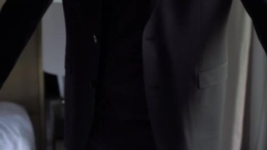 Takım elbisenin düğmelerini ilikleyen ellerin yakın çekimi. Adam siyah ceket giydi. Düğün günü damat ya da iş adamı. Beyaz gömlekli bir erkek..