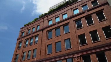 Bulutlu bir arkaplan altında parlak güneş ışığını yansıtan tarihi bir tuğla binanın büyüleyici manzarası.