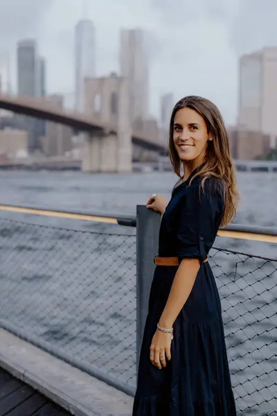 Şık ve modaya uygun bir kadın inanılmaz bir şehir manzarası olan güzel rıhtım kenarında güven içinde poz veriyor. New York 'taki Brooklyn Köprüsü.
