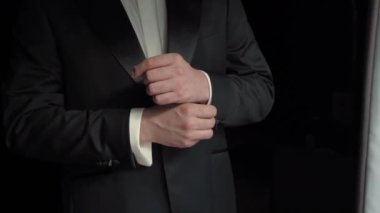 Kendinden emin bir adam parlayan kol düğmelerini ayarlar, resmi kıyafetlerini ve detaylara olan ilgisini gösterir.