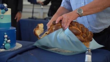 Canlı bir şenlik masasında güzel dekore edilmiş bir pastanın yanında ustalıkla örülmüş bir ekmek kesen bir el.