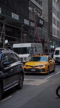 NEW YORK, ABD - 30 Mayıs 2024: Modern mimarinin arka planına karşı klasik sarı bir taksinin yer aldığı canlı bir New York caddesi.