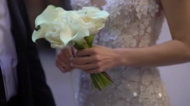 Çok güzel bir gelin. Karmaşık ve zarif bir elbise giymiş. Elinde baş döndürücü bir buket tutarken romantik anlar yakalıyor.