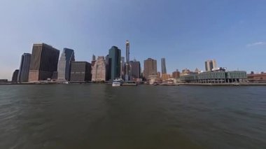 İkonik New York siluetinin berrak gökyüzüne ve sakin bir su ön planına karşı çarpıcı panoramik görüntüsü.