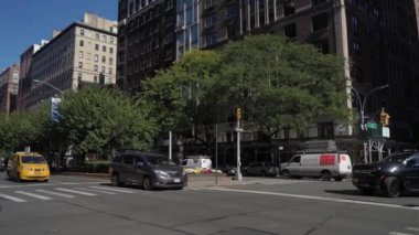 NEW YORK, ABD - 11 Ağustos 2024: Parlak sarı bir taksi çeşitli renkli çiçeklerle süslenmiş yemyeşil bir şehir parkının yanından hızla geçiyor