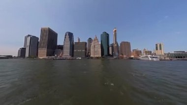 İkonik New York siluetinin berrak gökyüzüne ve sakin bir su ön planına karşı çarpıcı panoramik görüntüsü.