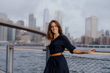 Şık ve modaya uygun bir kadın inanılmaz bir şehir manzarası olan güzel rıhtım kenarında güven içinde poz veriyor. New York 'taki Brooklyn Köprüsü.