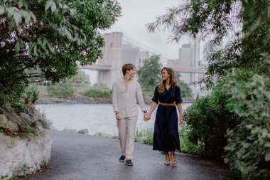 Bereketli yeşillik ve sükunetle çevrili bir rıhtım boyunca el ele dolaşan bir çiftin romantik bir sahnesi. New York 'taki Brooklyn Köprüsü.