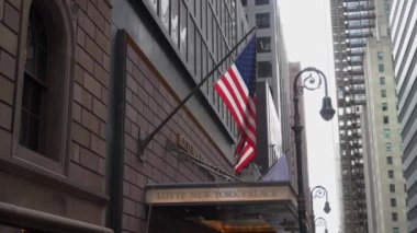 NEW YORK, ABD - 4 Nisan 2024: Bir Amerikan bayrağının gökdelenlerin arasında gururla dalgalandığı büyüleyici şehir manzarası. Lotte Oteli Girişi.