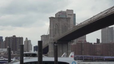NEW YORK, ABD - 20 Kasım 2024: İkonik Brooklyn Köprüsü canlı New York şehrinde bulutlu bir günde zarif bir şekilde suyun üzerinde uzanıyor