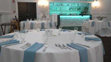 Güzel düzenlenmiş yemek seti, gösterişli şık masalar ve mavi ışıklarla aydınlatılmış şık bir bar.