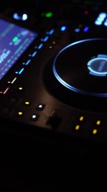 Bir DJ, loş bir gece kulübünde canlı ışıklarla aydınlatılmış profesyonel bir DJ konsolunda ustalıkla müziği karıştırır. Neon ışıkları ve dijital görüntüler dinamik bir görsel ortam yaratır..