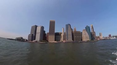 İkonik New York siluetinin berrak gökyüzüne ve sakin bir su ön planına karşı çarpıcı panoramik görüntüsü.