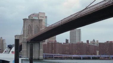 NEW YORK, ABD - 20 Kasım 2024: İkonik Brooklyn Köprüsü canlı New York şehrinde bulutlu bir günde zarif bir şekilde suyun üzerinde uzanıyor