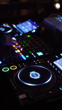 NEW YORK, ABD - 10 Şubat 2024: Bir DJ, loş bir gece kulübünde parlak ışıklarla aydınlatılmış profesyonel bir DJ konsolunda ustaca müziği karıştırıyor. Neon ışıkları ve dijital görüntüler