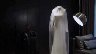 Güzel bir duvağı olan çarpıcı beyaz bir gelinlik şık bir ışıklandırma altında sergileniyor, zarafeti yakalıyor.