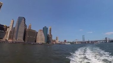 İkonik New York siluetinin berrak gökyüzüne ve sakin bir su ön planına karşı çarpıcı panoramik görüntüsü.