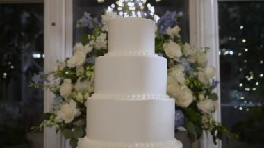 Göz kamaştırıcı beyaz bir düğün pastası çiçek aranjmanları ve ışıl ışıl bir avizeyle zarif bir şekilde sergileniyor..