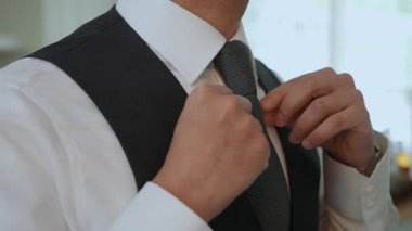 Bir adam şık kravatını resmi bir kıyafetle düzeltir. Görünüşünde zarafet ve entelektüellik gösterir.