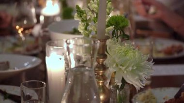 Göz kamaştırıcı çiçek süslemeleri ve yumuşak, sıcak mum ışığı içeren güzel bir yemek masası.