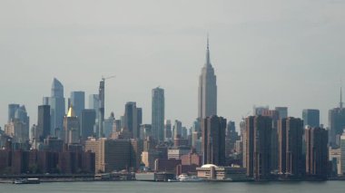 Bulutlu gökyüzünün altındaki New York siluetinin büyüleyici görüntüsü, ikonik binalar ve canlı bir deniz manzarası.