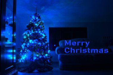 Üstünde mavi ışıklar olan bir pencerede Noel ağacı olan bir kartpostal. Mutlu Noeller yazılı. Üzerinde mavi ışıklar olan bir Noel ağacı olan bir kartpostal..