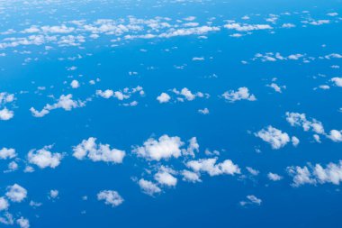 Mavi gökyüzü manzarası ve kabarık bulutlar, bir uçağın penceresinden çekilmiş bir resim..