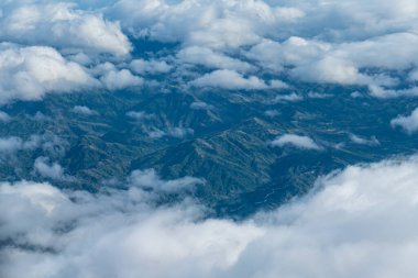 Kabarık bulutların ve karmaşık dağların görüntüsü, uçaktaki pencerelerden çekilen resimler.