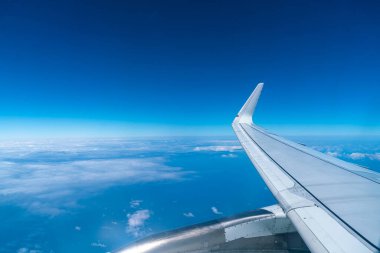 Mavi gökyüzü manzarası ve uçağın penceresinden kabarık bulutlar.