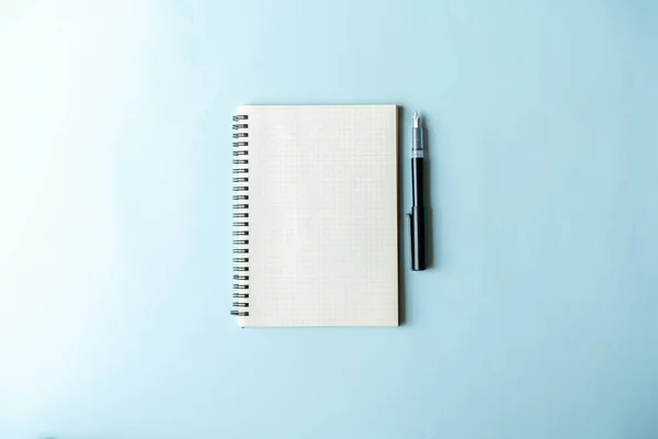 Cream paper notebook and black pen of office desktop with accessories on blue background ,Online learning design concept. Top view of  ,Top view with copy space for text