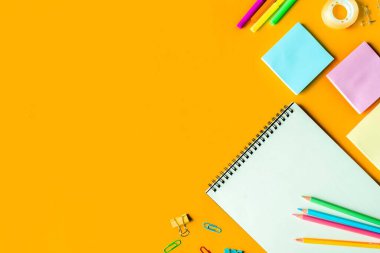 Üst görünüm fotoğrafı, okula dönüş konsepti, okul kırtasiyesiyle düz kompozisyon, renkli kalemler, boyalar, izole edilmiş sarı arkaplan üzerine not defteri, metin için metin alanı