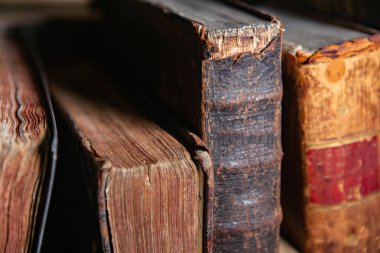 Kütüphanedeki raflarda duran çok eski kitaplar. Bilginin sembolü olarak kitaplar.