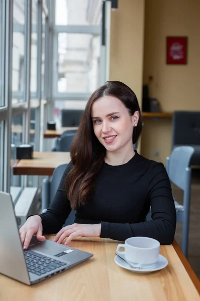 Beautiful businesswoman working on laptop in coffee shop. Female freelancer connecting to internet via computer. Blogger or journalist writing new article.