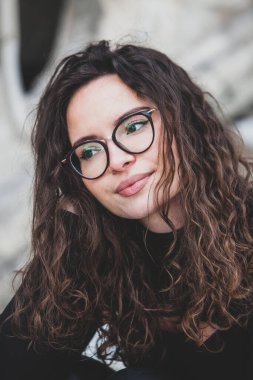 Esmer, kıvırcık saçlı, gözlüklü güzel bir kadın. Şehirde güneşin tadını çıkarıyor..