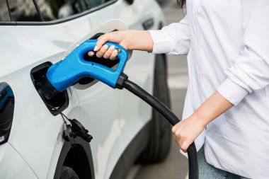 Genç bir iş kadını elektrikli arabasına EV şarj istasyonunda yakıt ikmali yapıyor. Çevre dostu araç kavramı. Elektrikli araba konsepti. Yeşil seyahat.