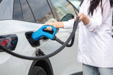 Genç bir iş kadını elektrikli arabasına EV şarj istasyonunda yakıt ikmali yapıyor. Çevre dostu araç kavramı. Elektrikli araba konsepti. Yeşil seyahat.