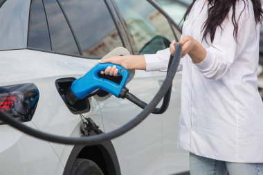 Genç bir iş kadını elektrikli arabasına EV şarj istasyonunda yakıt ikmali yapıyor. Çevre dostu araç kavramı. Elektrikli araba konsepti. Yeşil seyahat.