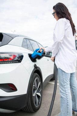 Genç bir iş kadını elektrikli arabasına EV şarj istasyonunda yakıt ikmali yapıyor. Çevre dostu araç kavramı. Elektrikli araba konsepti. Yeşil seyahat.