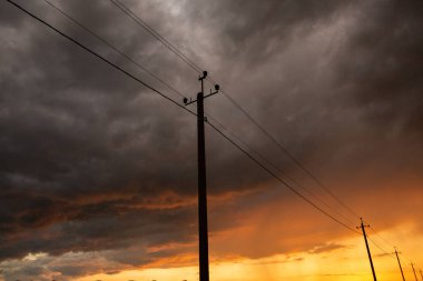 Gün batımında yüksek voltajlı elektrik hatları. Elektrik dağıtım istasyonu. Gökyüzünün arka planında elektrik direkleri