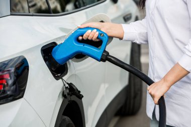 Genç bir iş kadını elektrikli arabasına EV şarj istasyonunda yakıt ikmali yapıyor. Çevre dostu araç kavramı. Elektrikli araba konsepti. Yeşil seyahat.
