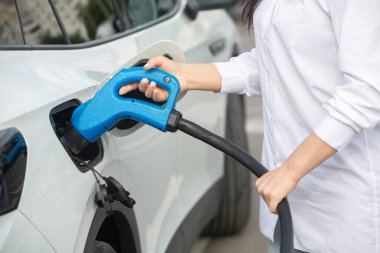 Genç bir iş kadını elektrikli arabasına EV şarj istasyonunda yakıt ikmali yapıyor. Çevre dostu araç kavramı. Elektrikli araba konsepti. Yeşil seyahat.