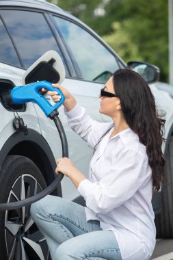 Genç bir iş kadını elektrikli arabasına EV şarj istasyonunda yakıt ikmali yapıyor. Çevre dostu araç kavramı. Elektrikli araba konsepti. Yeşil seyahat.