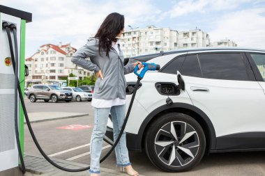 Genç bir iş kadını elektrikli arabasına EV şarj istasyonunda yakıt ikmali yapıyor. Çevre dostu araç kavramı. Elektrikli araba konsepti. Yeşil seyahat.