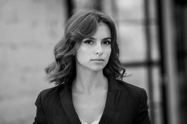 Uzun kahverengi saçlı, mavi ceketli, bir ofis binasının arka planında duran güzel bir genç kadının portresi. güçlü ve kendinden emin iş kadını