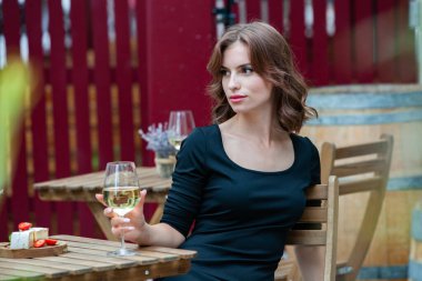 Güzel genç bir kadın bir restoranın terasında beyaz şarap içiyor.