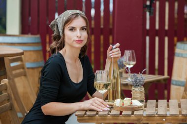 Güzel genç bir kadın bir restoranın terasında beyaz şarap içiyor.