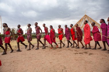 Masai geleneksel renkli giysiler içinde Masai 'nin ünlü Safari seyahat merkezinin yakınındaki yerel bir kabile köyünde dans ettiğini gösteriyor. Kenya. Yazı