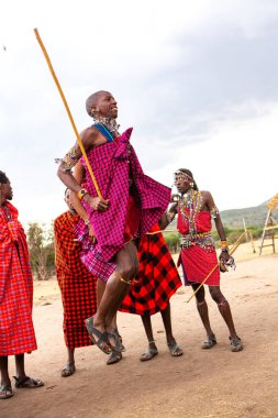 Masai geleneksel renkli giysiler içinde Masai 'nin ünlü Safari seyahat merkezinin yakınındaki yerel bir kabile köyünde dans ettiğini gösteriyor. Kenya. Yazı